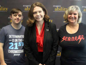 Sean and Sandra McElwee posing for a photo with RespectAbility Fellow Theresa Maher in front of a RespectAbility banner