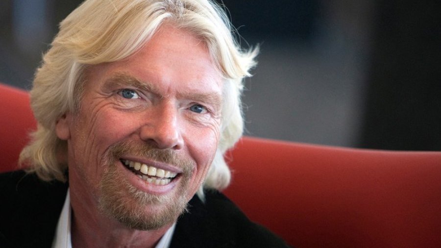 Richard Branson seated on a red couch, smiling and facing the camera