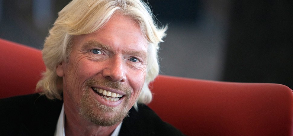 Richard Branson seated on a red couch, smiling and facing the camera