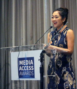 Atypical's Amy Okuda standing at a podium with the sign Media Access Awards