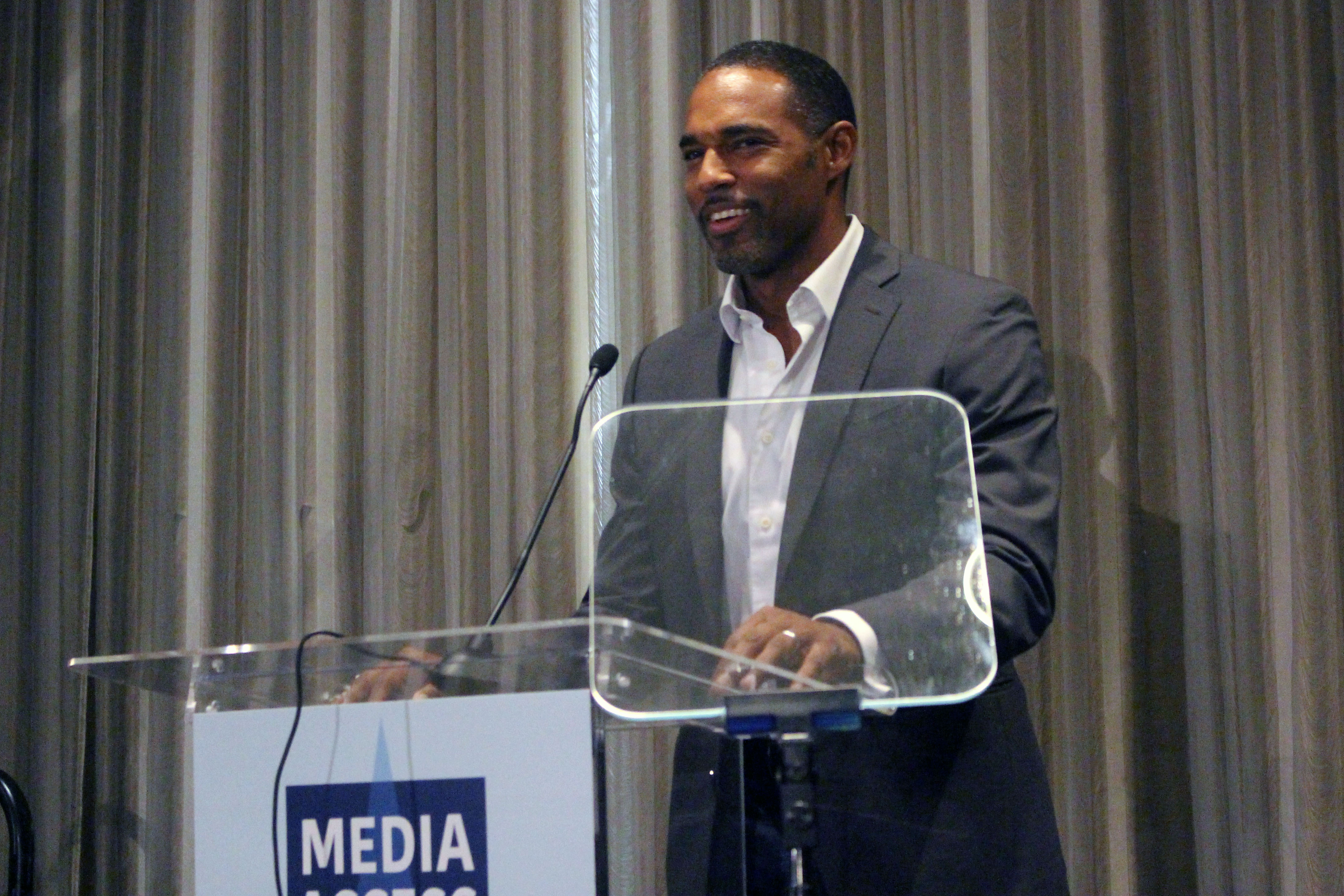 Jason George standing at a podium with the sign Media Access Awards