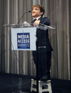 Nic Novicki standing at a podium with the sign Media Access Awards