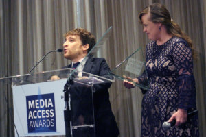 Nic Novicki and Jamie Brewer standing at a podium with the sign Media Access Awards