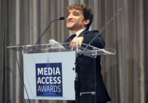 Nic Novicki standing at a podium with the sign Media Access Awards