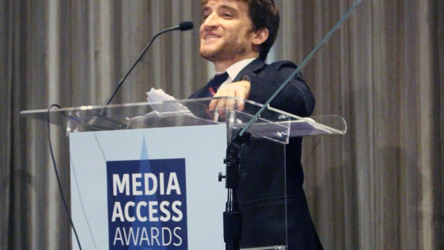 Nic Novicki standing at a podium with the sign Media Access Awards