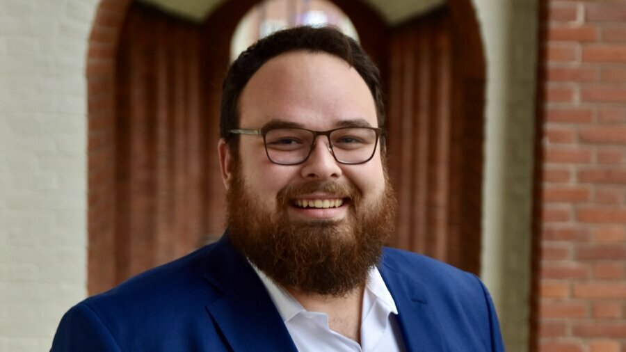 Ben Bond smiling headshot in front of a blurred background wearing a blue suit jacket.