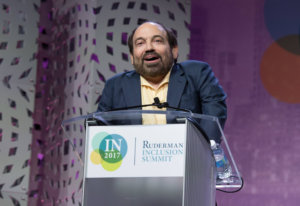 Danny Woodburn standing behind a podium with a sign saying Ruderman Inclusion Summit