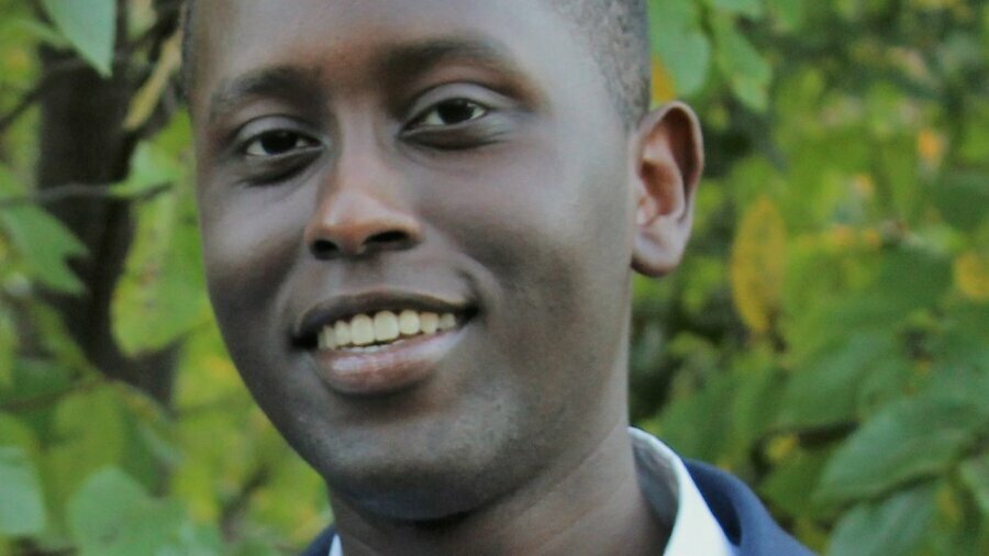 Ian Cherutich smiling wearing a navy blue suit in front of trees and bushes outside