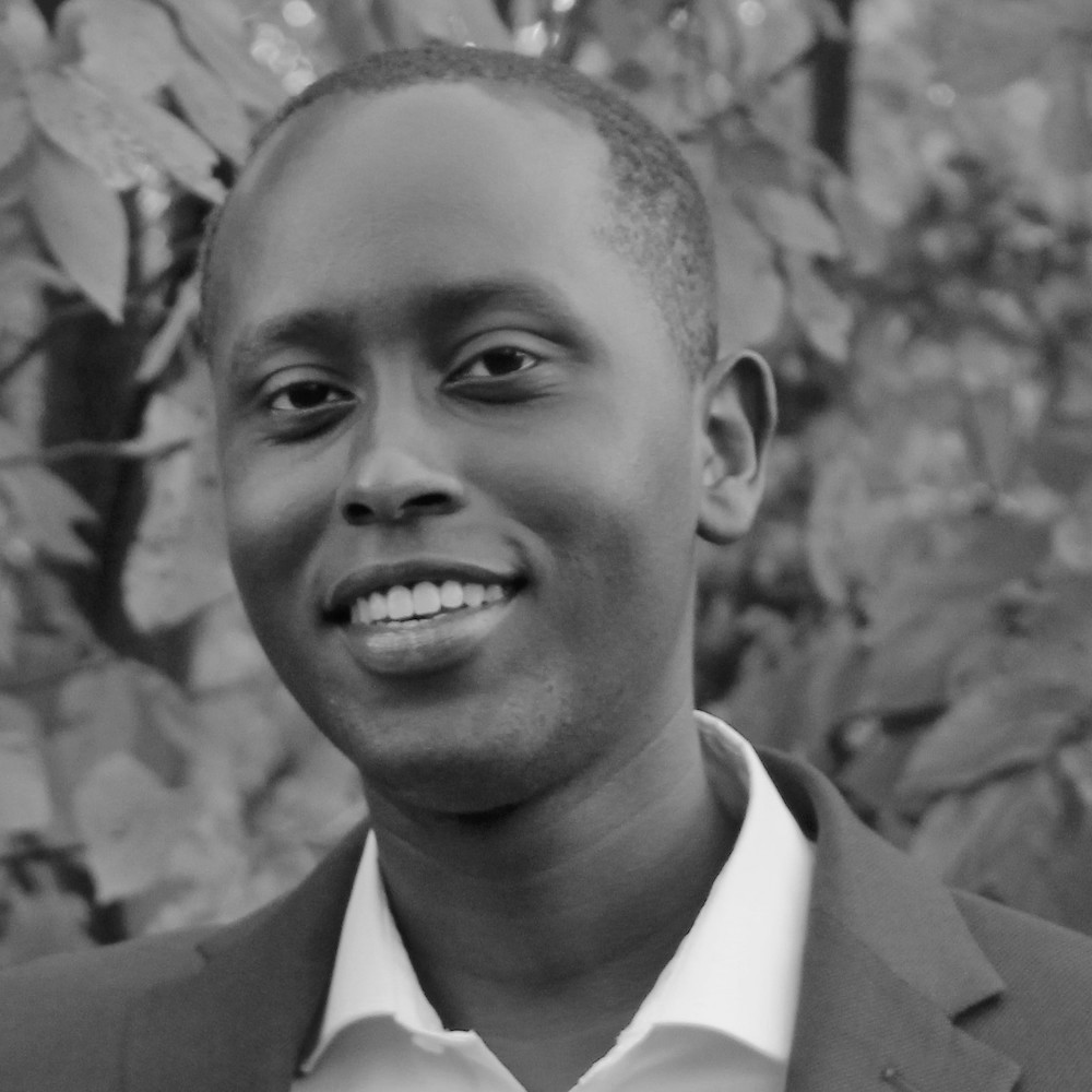 Ian Cherutich smiling wearing a suit in front of trees and bushes outside