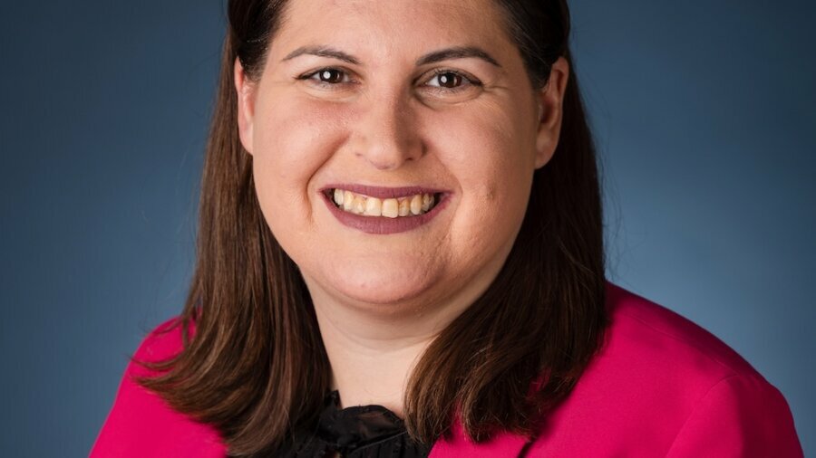 Lauren Appelbaum smiling headshot wearing a pink suit jacket in front of a blue gradient backdrop