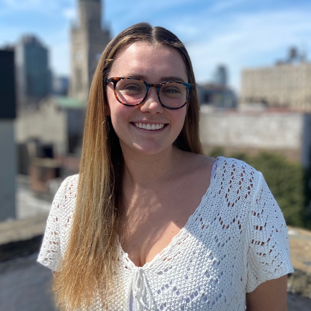 Molly McConville smiling headshot with a blurred city background behind her