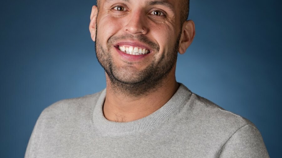 Phillip Saldana smiling headshot in front of a blue gradient backdrop