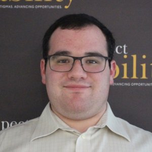 RespectAbility Fellow Eric Ascher smiling in front of the RespectAbility banner