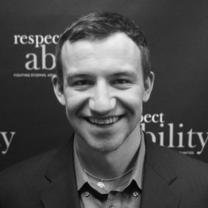 RespectAbility Fellow Nicholas Olson smiling in front of the RespectAbility banner