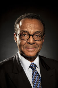 Clarence Page headshot wearing black suit, white shirt and glasses