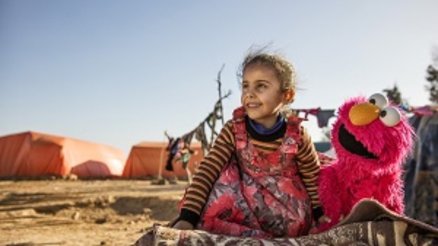 A young girl engages with Elmo at an informal tented settlement near Mafraq, Jordan, in February 2017