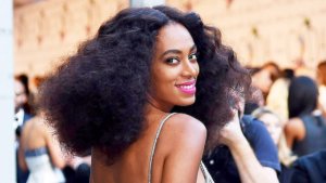 headshot of Solange Knowles wearing a gold dress and pink lipstick