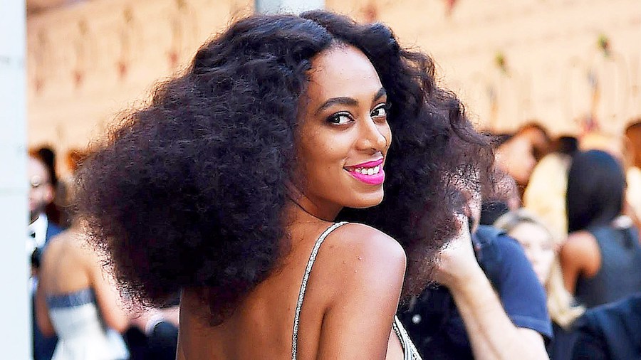 headshot of Solange Knowles wearing a gold dress and pink lipstick