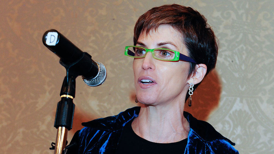Deborah Calla wearing green glasses behind a microphone
