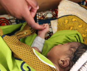 An adult finger holding the hand of a baby that is lying down on a blanket.