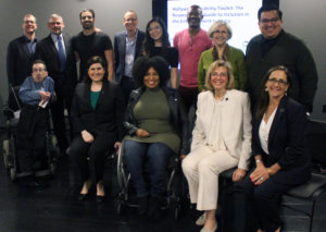 A group of people seated in chairs and wheelchairs and standing smiling and posing for the camera