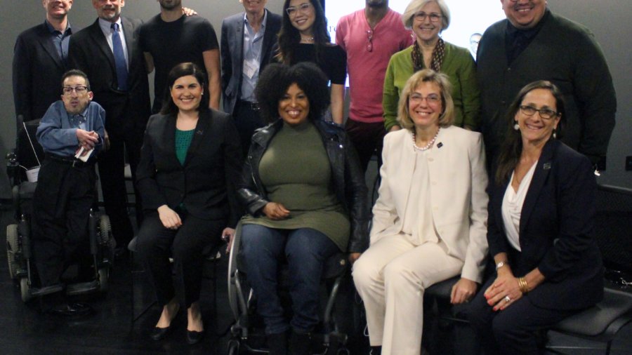 A group of people seated in chairs and wheelchairs and standing smiling and posing for the camera