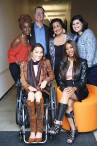five diverse women and one man standing and seated smiling for the camera