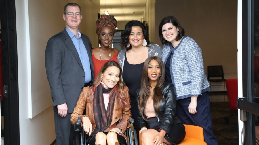 five diverse women and one man standing and seated smiling for the camera