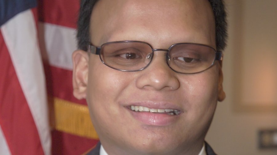 Ollie Cantos smiling in front of an American flag