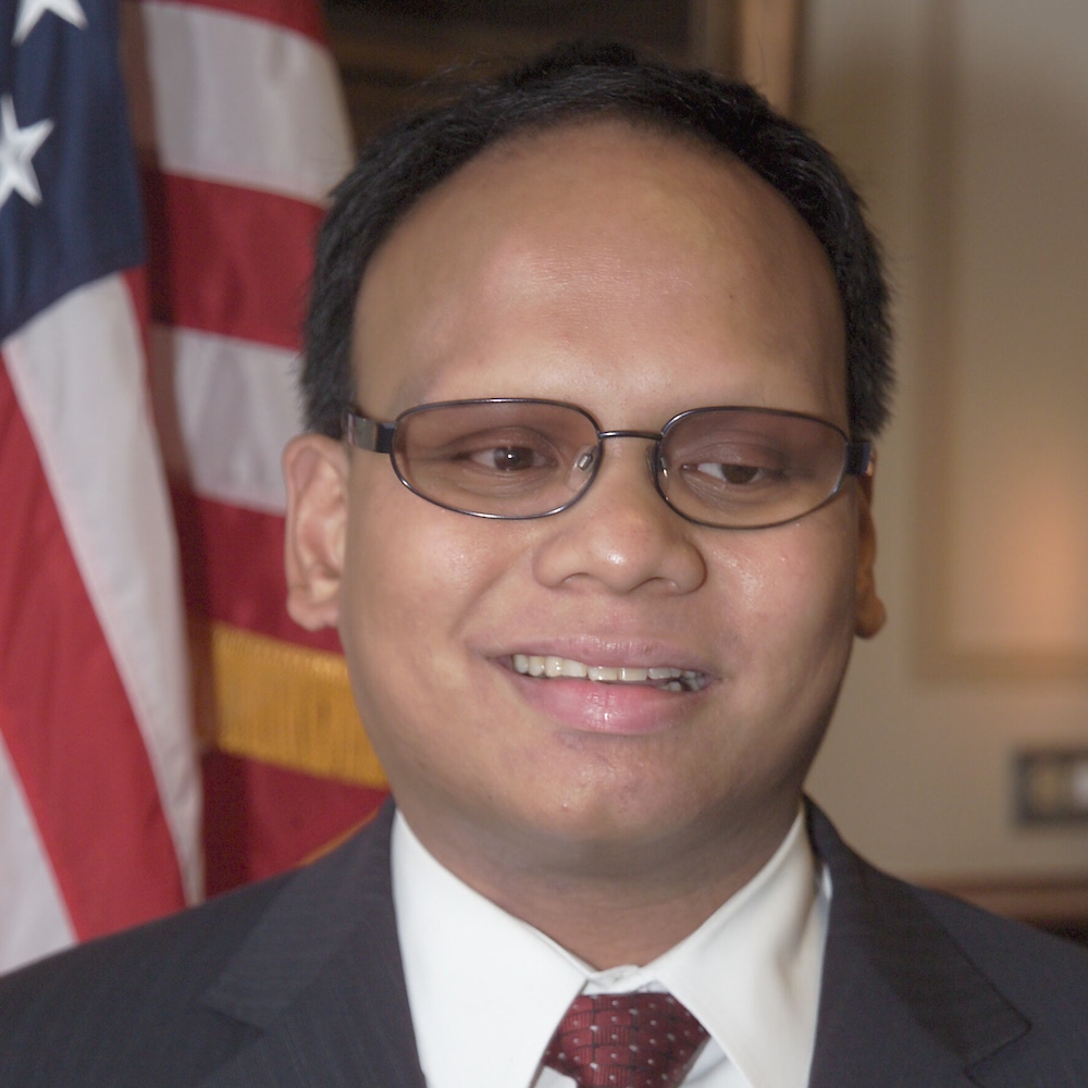 Ollie Cantos smiling in front of an American flag