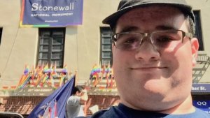 Former RespectAbility Fellow Eric Ascher in front of the Stonewall Inn in New York City with a banner reading "Stonewall National Monument #findyourpark"