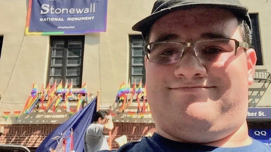 Former RespectAbility Fellow Eric Ascher in front of the Stonewall Inn in New York City with a banner reading 