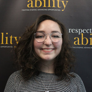 Rachael Walloga is smiling in front of the RespectAbility banner