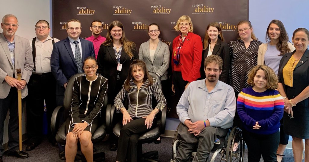 Vivian Bass with RespectAbility Staff and Fellows in front of the RespectAbility banner