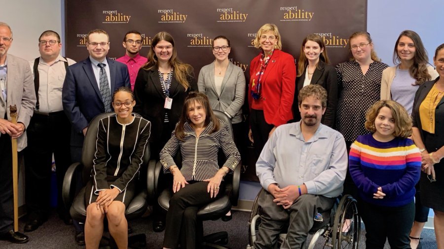 Vivian Bass with RespectAbility Staff and Fellows in front of the RespectAbility banner