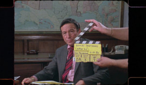 Mike Wallace about to start filming a 60 minutes piece, sitting in front of a world map with the director holding the clapperboard