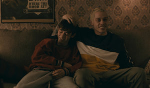 Griffin Gluck and Pete Davidson sitting on a couch. Pete has his hand on Griffin's head