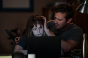 Dakota Johnson and Armie Hammer sit in front of a laptop. Armie is holding a knife and petting Dakota's hair