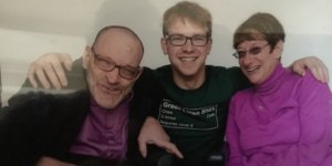 L-R: Neil Jacobson, David Jacobson and Denise Jacobson smiling together. David has his arms around Neil and Denise.