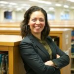 Shirley Leyro smiling in front of bookshelves in a library