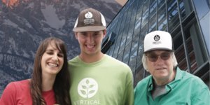 Three stars of Hearts of Glass smiling together in front of mountains and a greenhouse holding plants.