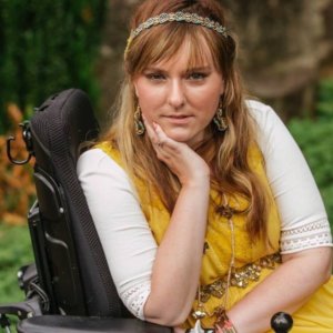 Ariella Barker in front of a tree and bushes. Ariella is a wheelchair user