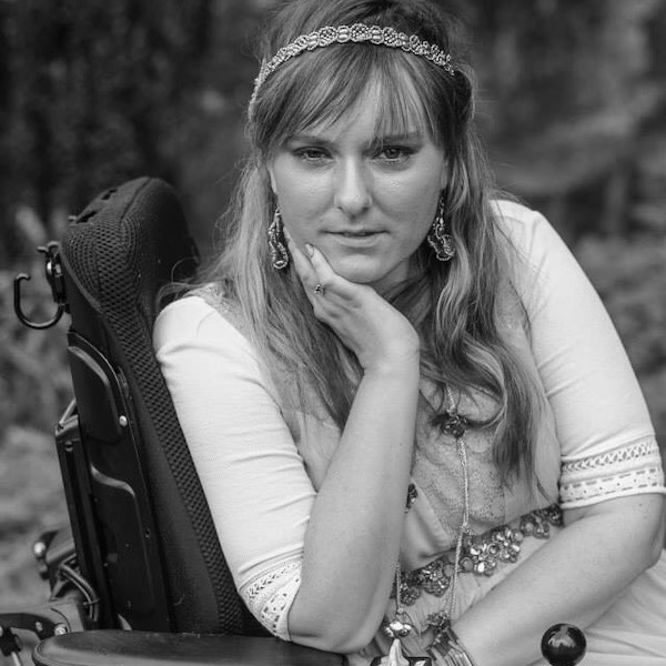 Ariella Barker in front of a tree and bushes. Ariella is a wheelchair user