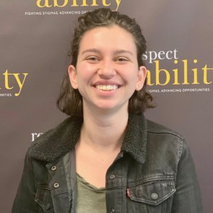 Charlotte Ruda smiling in front of the RespectAbility banner