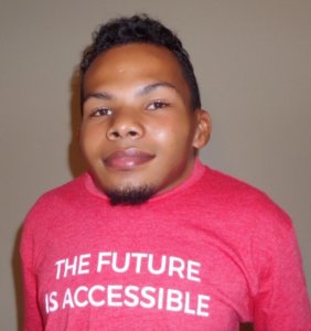 Justin Tapp smiling wearing a pink t shirt that says "The Future Is Accessible"