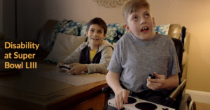 Still from Microsoft Commercial with two young boys playing video games, one of whom is a wheelchair user and playing with their adaptive controller. Text: Disability at Super Bowl LIII