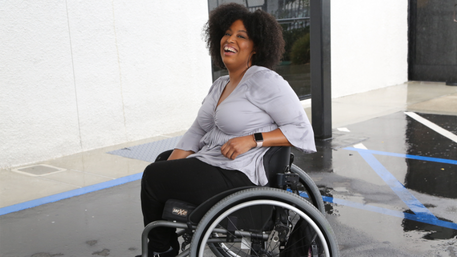 Tatiana Lee smiling in a parking lot. Tatiana is a wheelchair user.