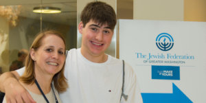 Lisa Handelman smiles with a young adult with a disability in front of a sign for The Jewish Federation of Greater Washington