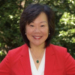 Frances West wearing a red jacket smiling in front of trees