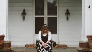 Ariella Barker sitting in a wheelchair in front of her house, looking down